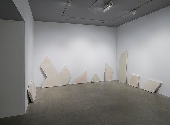 A concrete bench sculpture, made of geometric shapes with a triangle sticking up from the seat area, sits on a gray gallery floor.